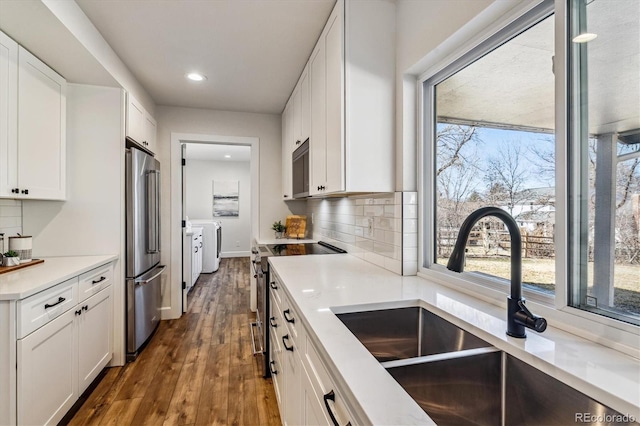 kitchen featuring decorative backsplash, white cabinets, washer and dryer, stainless steel appliances, and a sink