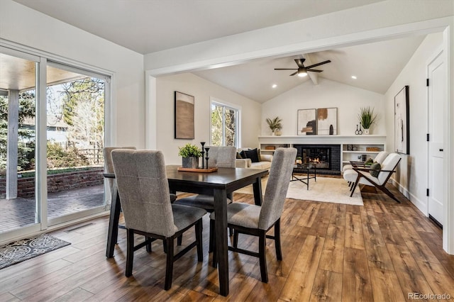 dining space with hardwood / wood-style floors, vaulted ceiling with beams, a fireplace, and a ceiling fan