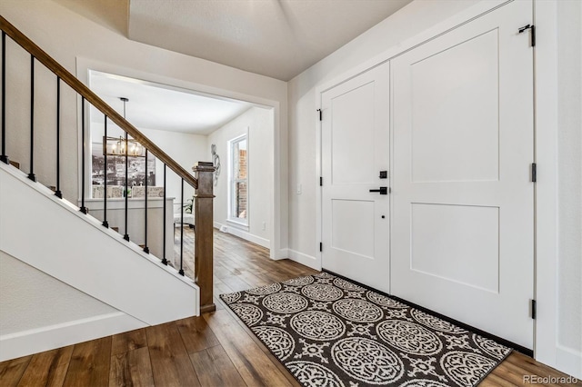 entryway featuring baseboards, an inviting chandelier, hardwood / wood-style floors, and stairs