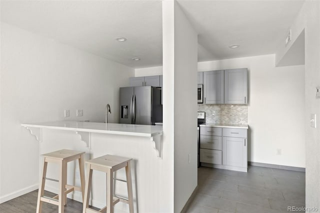3550 S Harlan St Unit 363, Denver, CO 80235 - kitchen with appliances with stainless steel finishes, gray cabinetry, a breakfast bar area, decorative backsplash, and recessed lighting
