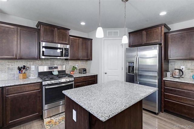 10869 Traders Pkwy, Fountain, CO 80817 - kitchen featuring appliances with stainless steel finishes, light wood finished floors, dark brown cabinets, decorative backsplash, and a kitchen island