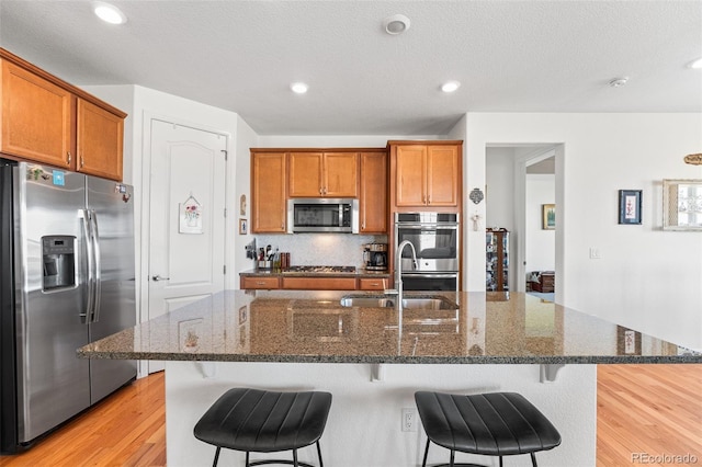 14805 Quince Way, Thornton, CO 80602 - kitchen with stainless steel appliances, light wood-style flooring, brown cabinets, a breakfast bar area, and dark stone counters
