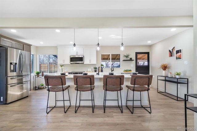 kitchen with hanging light fixtures, light wood-type flooring, appliances with stainless steel finishes, a kitchen island, and white cabinetry