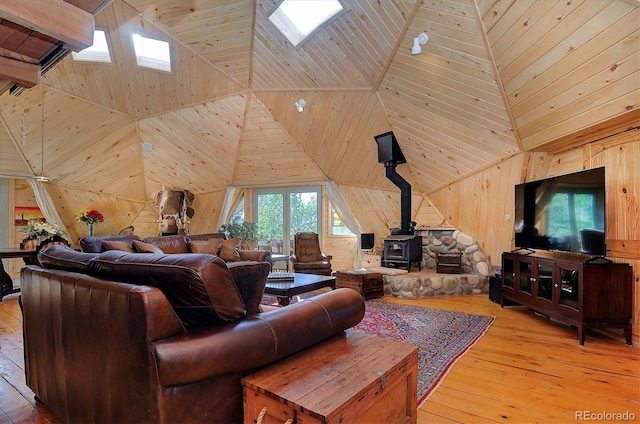 living room featuring high vaulted ceiling, a skylight, wood walls, and a wood stove