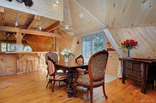 dining area with wood-type flooring, wooden walls, vaulted ceiling with beams, and wooden ceiling