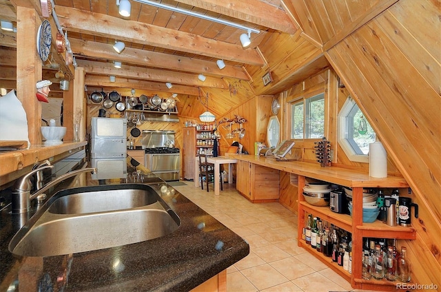 kitchen featuring beamed ceiling, wooden walls, light tile patterned floors, sink, and wooden ceiling