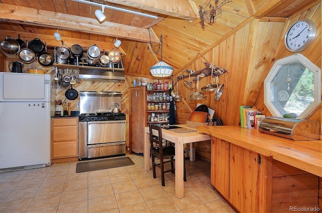 kitchen with light tile patterned floors, wooden walls, beamed ceiling, stainless steel gas range, and white fridge