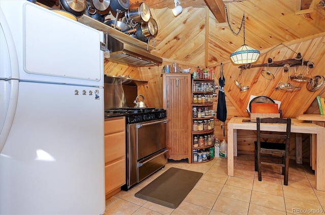 kitchen featuring wooden walls, white fridge, range with gas cooktop, vaulted ceiling, and light tile patterned flooring