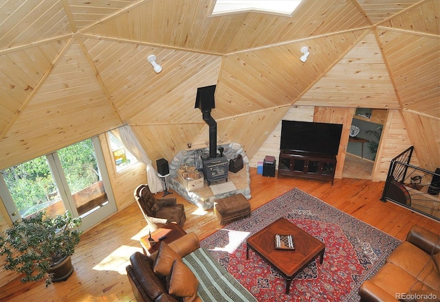 living room featuring hardwood / wood-style flooring, wooden walls, lofted ceiling with skylight, wood ceiling, and a wood stove