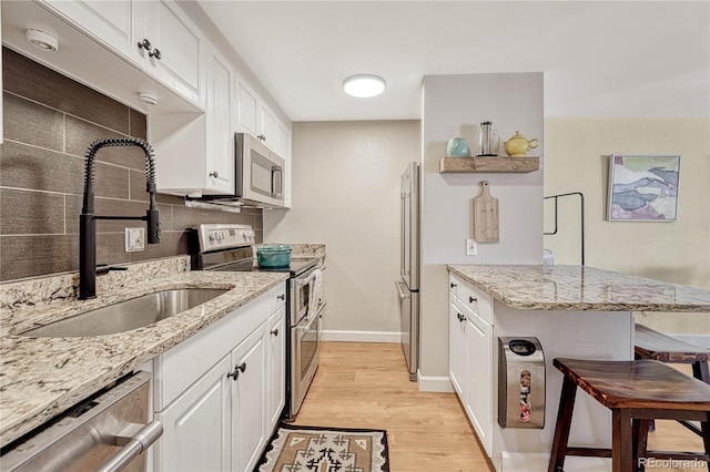 kitchen with white cabinets, sink, light stone countertops, light hardwood / wood-style floors, and stainless steel appliances