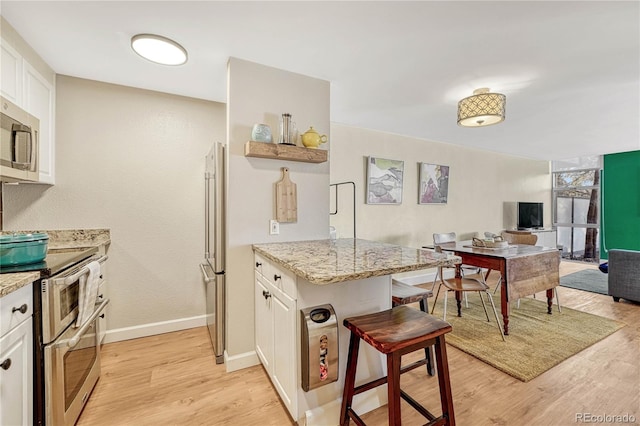 kitchen with light hardwood / wood-style flooring, appliances with stainless steel finishes, light stone countertops, white cabinets, and kitchen peninsula