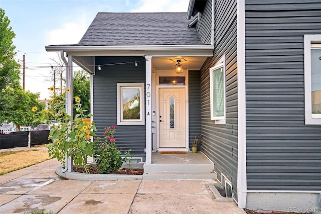 view of exterior entry with roof with shingles