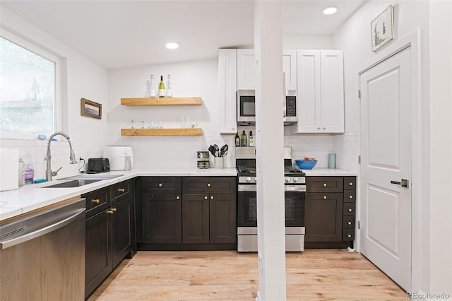 kitchen with light wood-type flooring, a sink, backsplash, white cabinetry, and appliances with stainless steel finishes