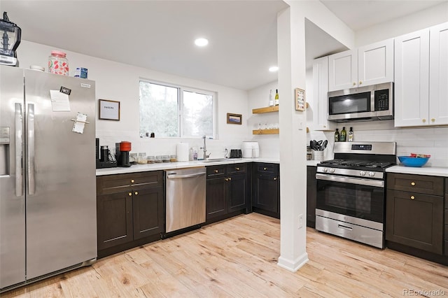 kitchen with open shelves, light wood-style flooring, stainless steel appliances, light countertops, and tasteful backsplash