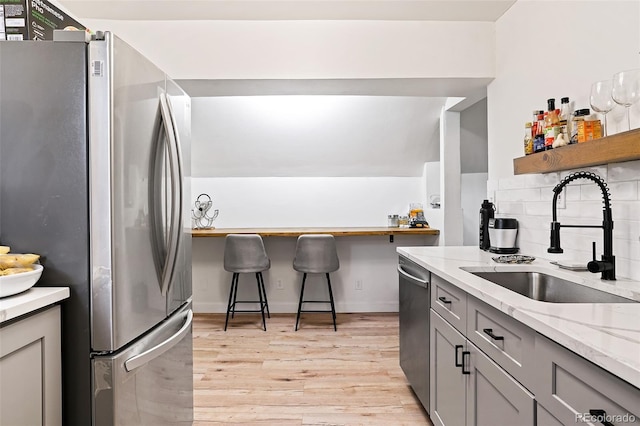 kitchen with gray cabinets, a sink, tasteful backsplash, stainless steel appliances, and light wood-style floors