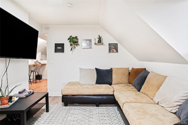 living area with vaulted ceiling, baseboards, and light wood-type flooring