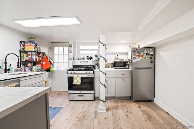 kitchen with gray cabinetry, baseboards, light wood-style flooring, appliances with stainless steel finishes, and a sink