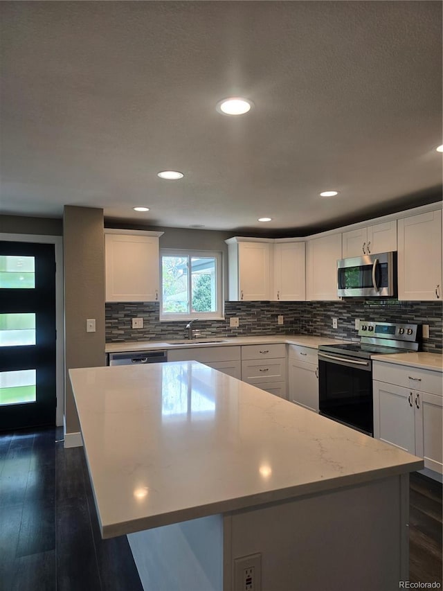 795 Vivian Ct, Lakewood, CO 80401 - kitchen with appliances with stainless steel finishes, a center island, a sink, decorative backsplash, and white cabinetry