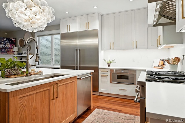 549 Milwaukee St, Denver, CO 80206 - kitchen featuring wall chimney exhaust hood, appliances with stainless steel finishes, wood finished floors, light countertops, and recessed lighting
