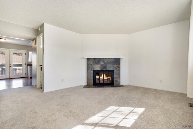 unfurnished living room with a tiled fireplace, french doors, a textured ceiling, and carpet