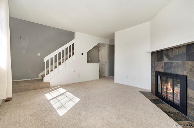 unfurnished living room with a fireplace, stairs, and carpet