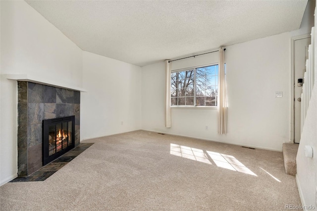 unfurnished living room featuring visible vents, a tile fireplace, a textured ceiling, and carpet floors