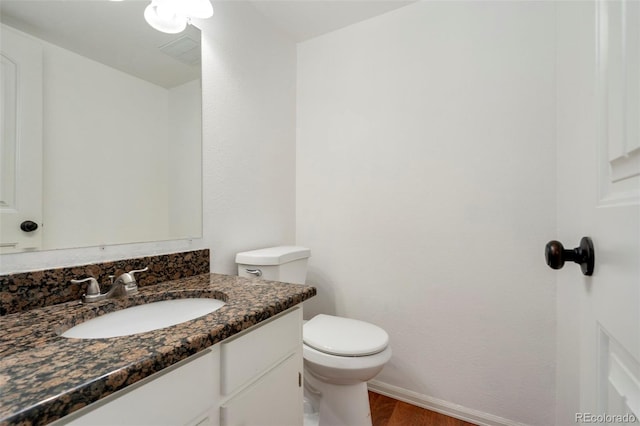 half bath with toilet, vanity, baseboards, and wood finished floors