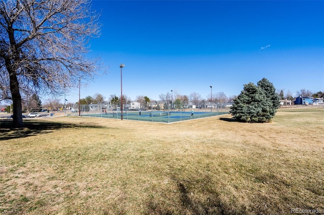 view of home's community featuring a lawn, a tennis court, and fence