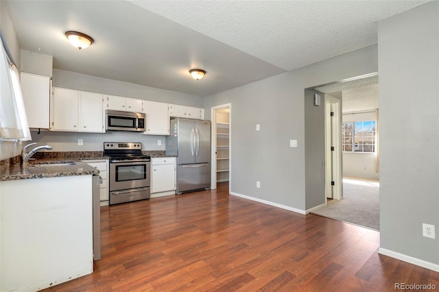 kitchen featuring dark stone countertops, baseboards, dark wood finished floors, stainless steel appliances, and white cabinets