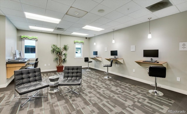 interior space featuring dark colored carpet, built in desk, and a drop ceiling