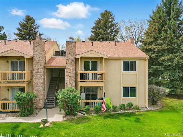 back of property featuring stucco siding, a balcony, a chimney, a lawn, and a shingled roof