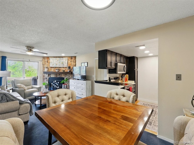 dining room with a textured ceiling, baseboards, ceiling fan, and a stone fireplace