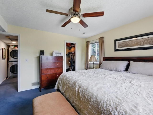 carpeted bedroom featuring estacked washer and dryer, a walk in closet, a closet, baseboards, and ceiling fan