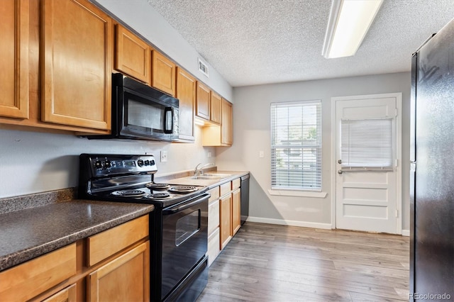 kitchen with a textured ceiling, light wood-type flooring, sink, and black appliances