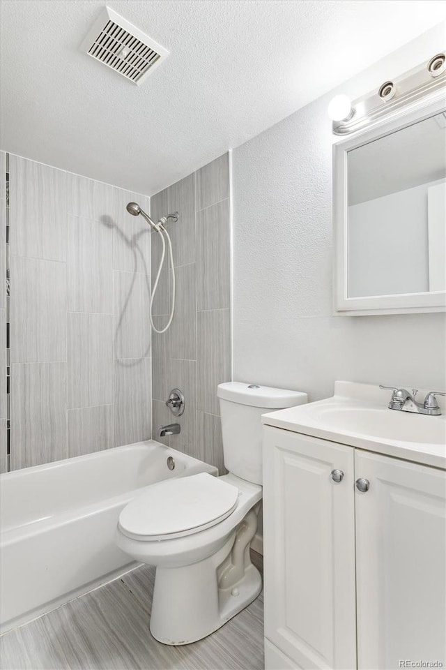 full bathroom with vanity, tiled shower / bath combo, a textured ceiling, hardwood / wood-style flooring, and toilet