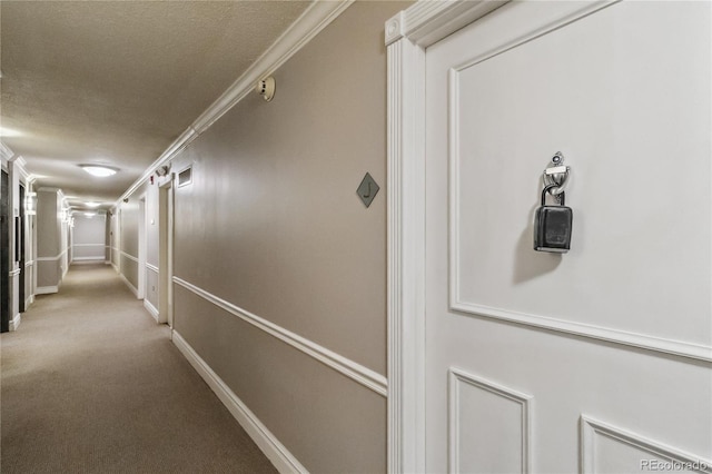 hall with ornamental molding, a textured ceiling, baseboards, and carpet floors