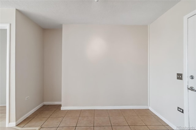 empty room featuring light tile patterned floors, baseboards, and a textured ceiling