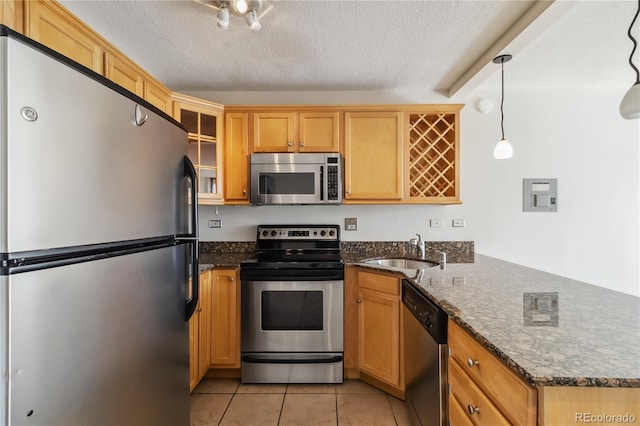 kitchen with light tile patterned floors, a peninsula, a sink, stainless steel appliances, and a textured ceiling