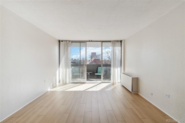 spare room with light wood-style floors, radiator, floor to ceiling windows, and a textured ceiling