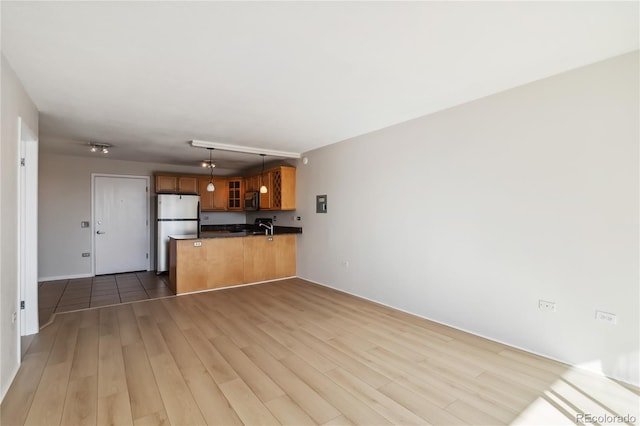 kitchen with stainless steel microwave, glass insert cabinets, a peninsula, freestanding refrigerator, and brown cabinetry