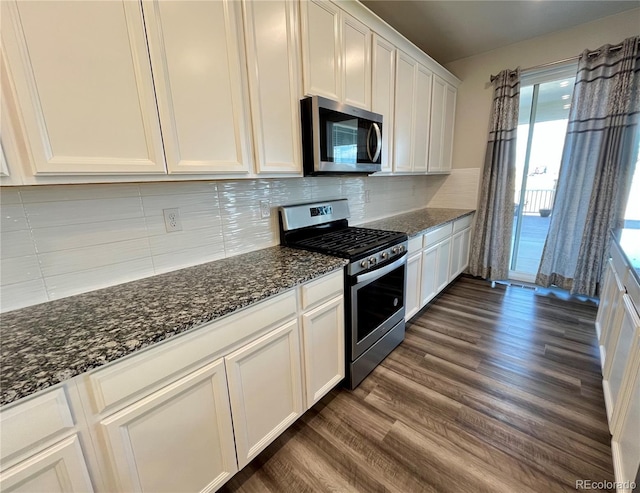 kitchen with white cabinets, dark stone counters, dark wood-style flooring, stainless steel appliances, and backsplash