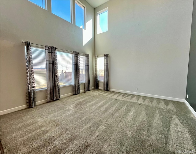 unfurnished living room featuring plenty of natural light, carpet flooring, a towering ceiling, and baseboards