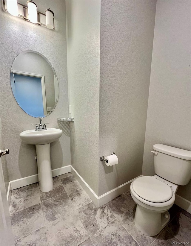 half bathroom with baseboards, a textured wall, and toilet