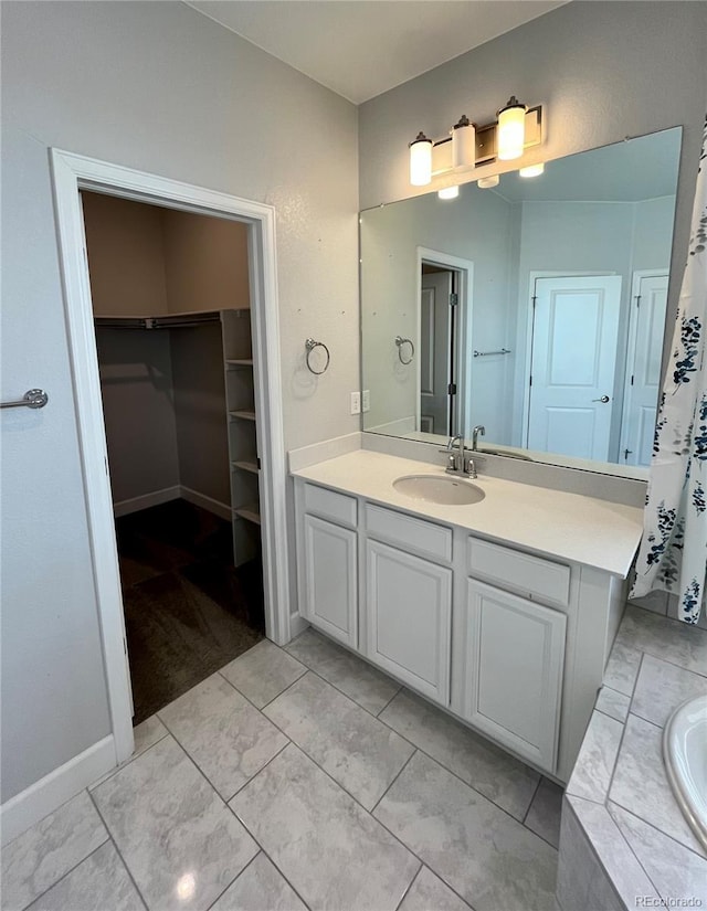 bathroom with a relaxing tiled tub, vanity, baseboards, and a spacious closet