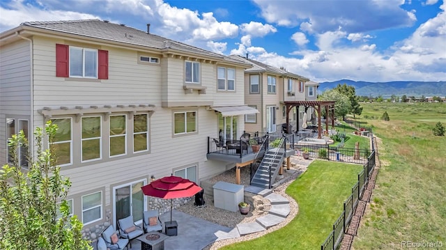 rear view of property featuring a lawn, a deck with mountain view, and a patio