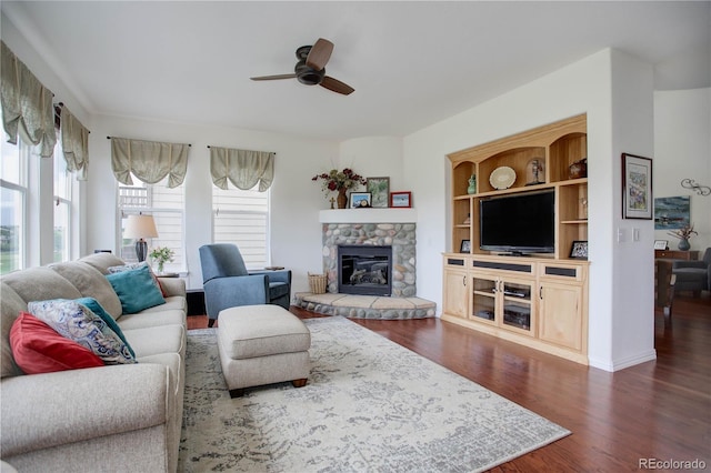 living room featuring ceiling fan, a stone fireplace, dark hardwood / wood-style flooring, and built in features