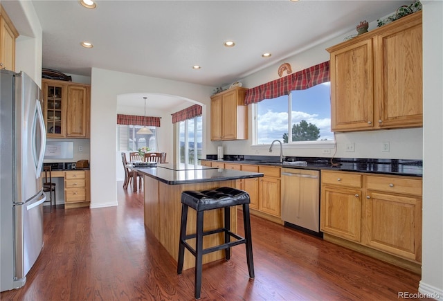 kitchen with appliances with stainless steel finishes, a kitchen breakfast bar, dark wood-type flooring, sink, and a center island