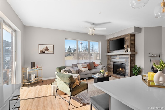 living room with ceiling fan, a large fireplace, a wealth of natural light, and light wood-type flooring