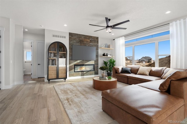 living room with light hardwood / wood-style flooring, a textured ceiling, built in features, ceiling fan, and a tiled fireplace