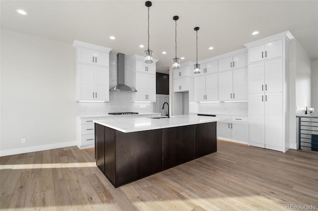 kitchen with a spacious island, sink, white cabinets, and wall chimney exhaust hood